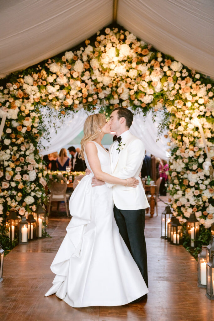 bride & groom kissing in front of Fall floral entryway arch by Emily Wren Photography