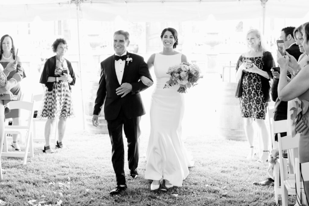 bride walking down the aisle during outdoor wedding ceremony under a white tent