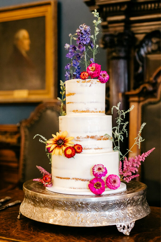 three tier half naked wedding cake with vibrant floral decor by Emily Wren Photography