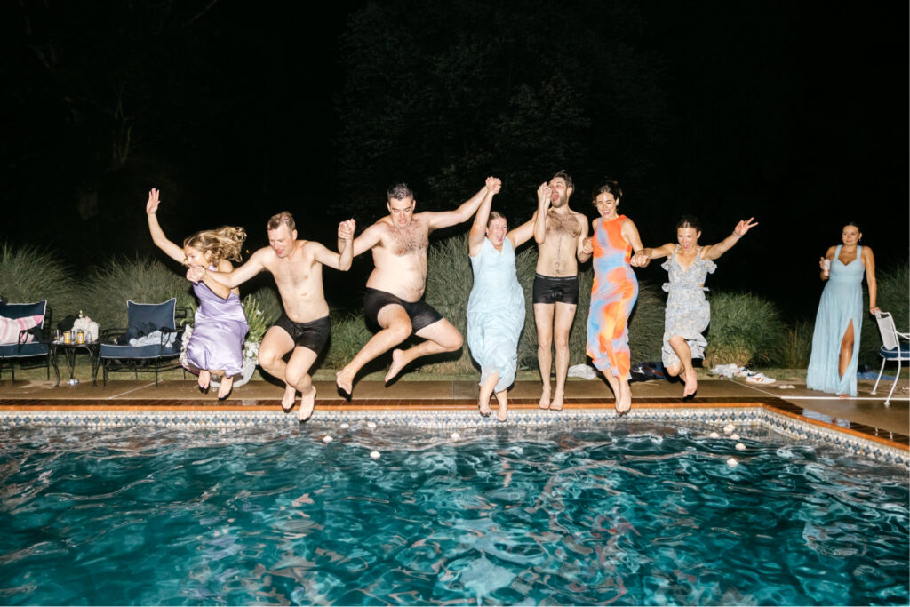 wedding guests jumping into a pool during the wedding reception by Emily Wren Photography