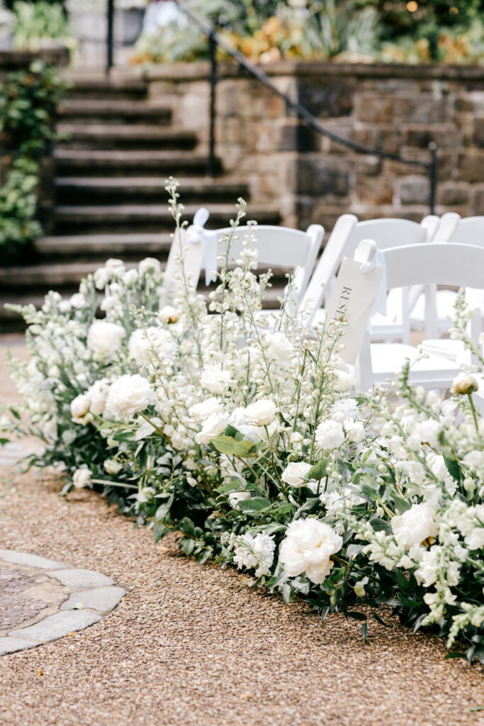 all white floral decor aligning wedding ceremony aisle