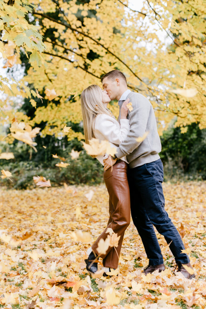 couple kissing as Autumn leaves fall around them in Philadelphia during their perfect fall engagement photoshoot by Emily Wren Photography