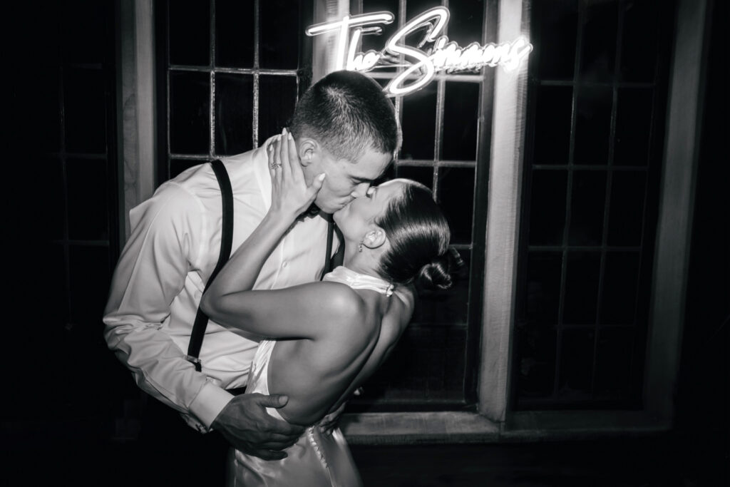 bride & groom kissing in front of LED sign with their last name by Emily Wren Photography