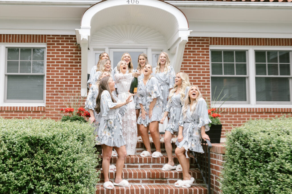 bride popping champagne with her bridesmaids on her summer New Jersey wedding day by Emily Wren Photography