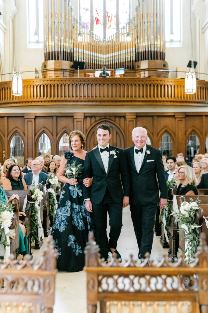 groom walking down the aisle with both of his parents at his wedding ceremony