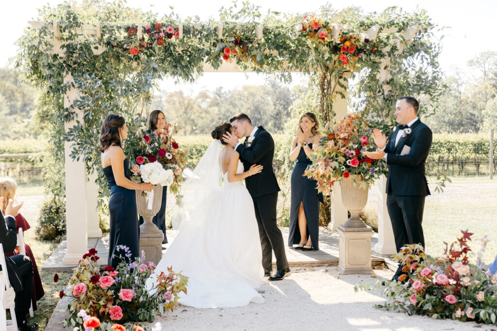 bride & grooms first kiss at their outdoor fall wedding ceremony at The Inn at Grace Winery in Glen Mills, Pennsylvania