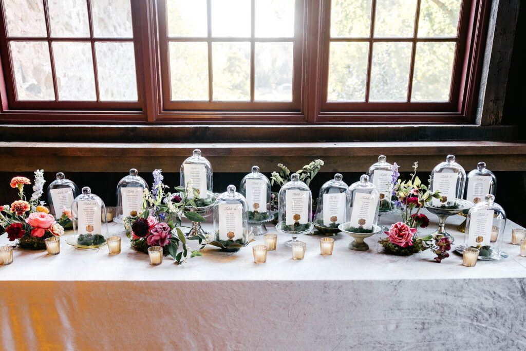 glass cloches, surrounded by fresh floral accents and moss wedding reception seating chart