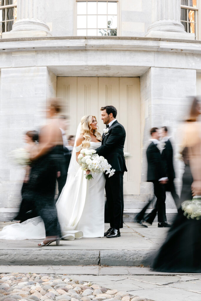 Bride and groom at Merchant's Exchange, while their wedding party walks around them by Emily Wren Photography