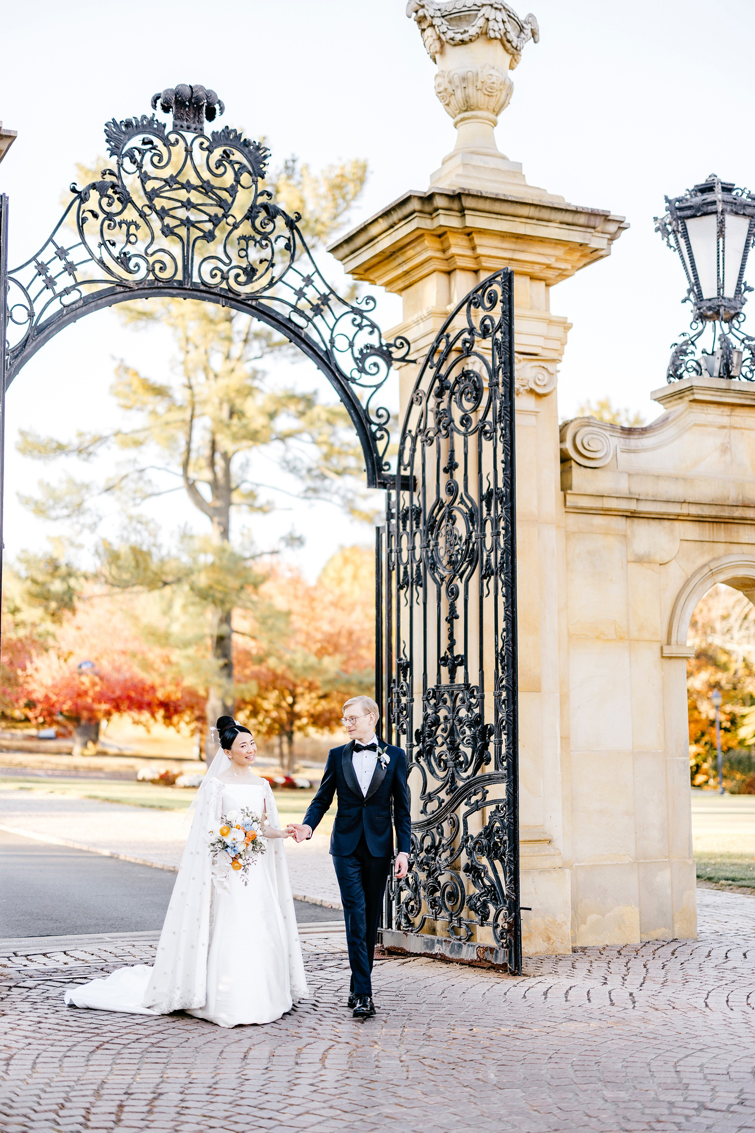 bride and groom walking through the gates at Jasna Polana on fall wedding day in New Jersey