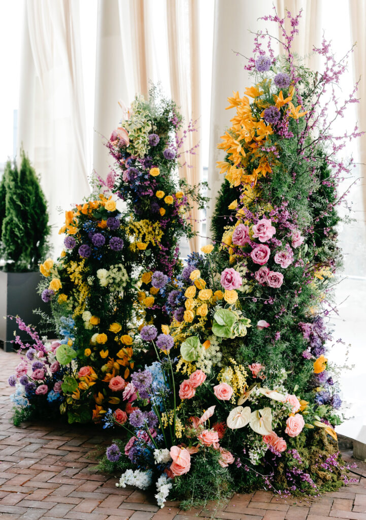colorful and vibrant wedding ceremony arch filled with purple, yellow, blue & pink flowers