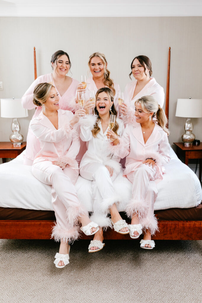 Bride drinking champagne with her bridesmaids in matching pink & white pajamas