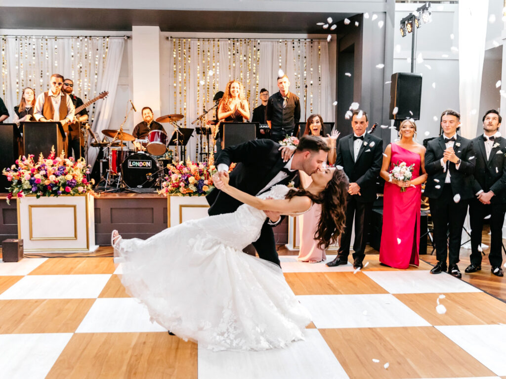 bride and groom kissing during their first dance as guests throw flower petals by Emily Wren Photography