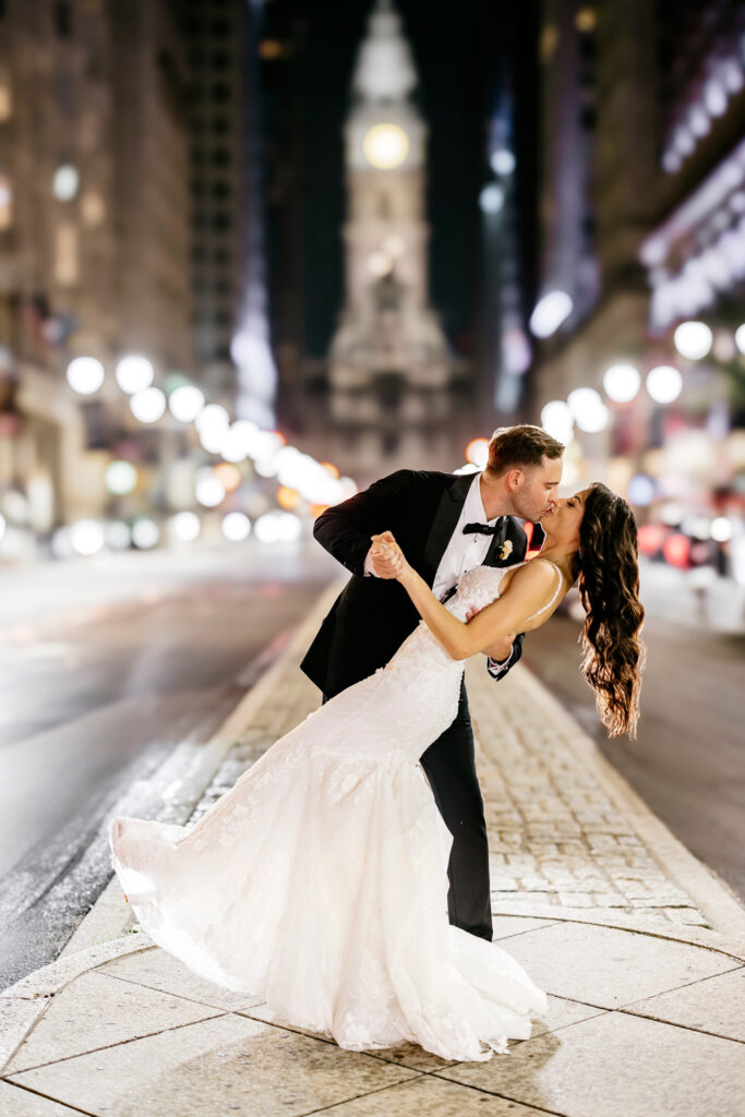 night portrait of bride and groom kissing in front of Philadelphia's city hall on broad street by luxurious wedding photographer Emily Wren Photography