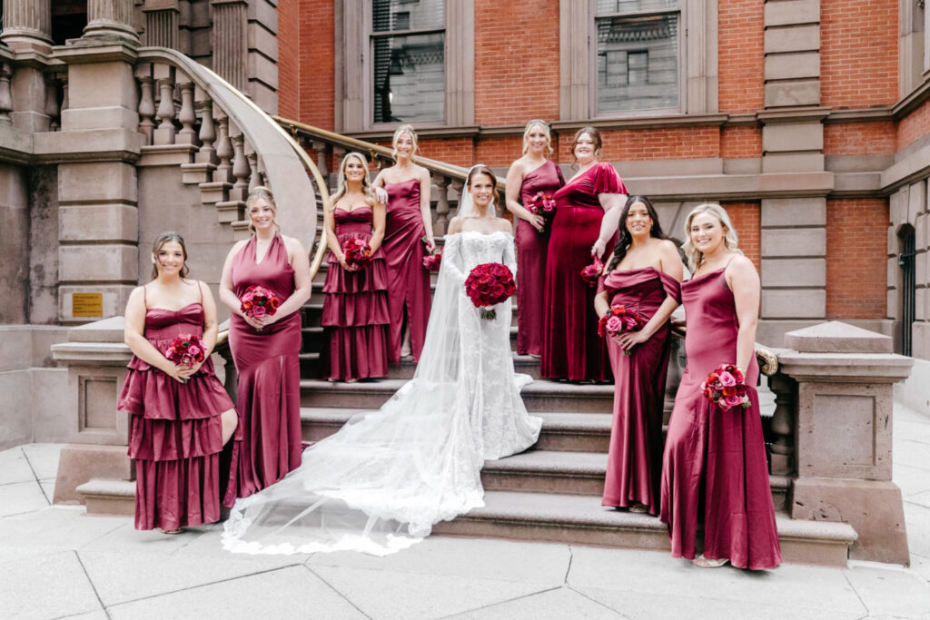 Philadelphia bride with her bridesmaids in matching velvet red bridesmaid dresses on the stairs leading up to the Union League