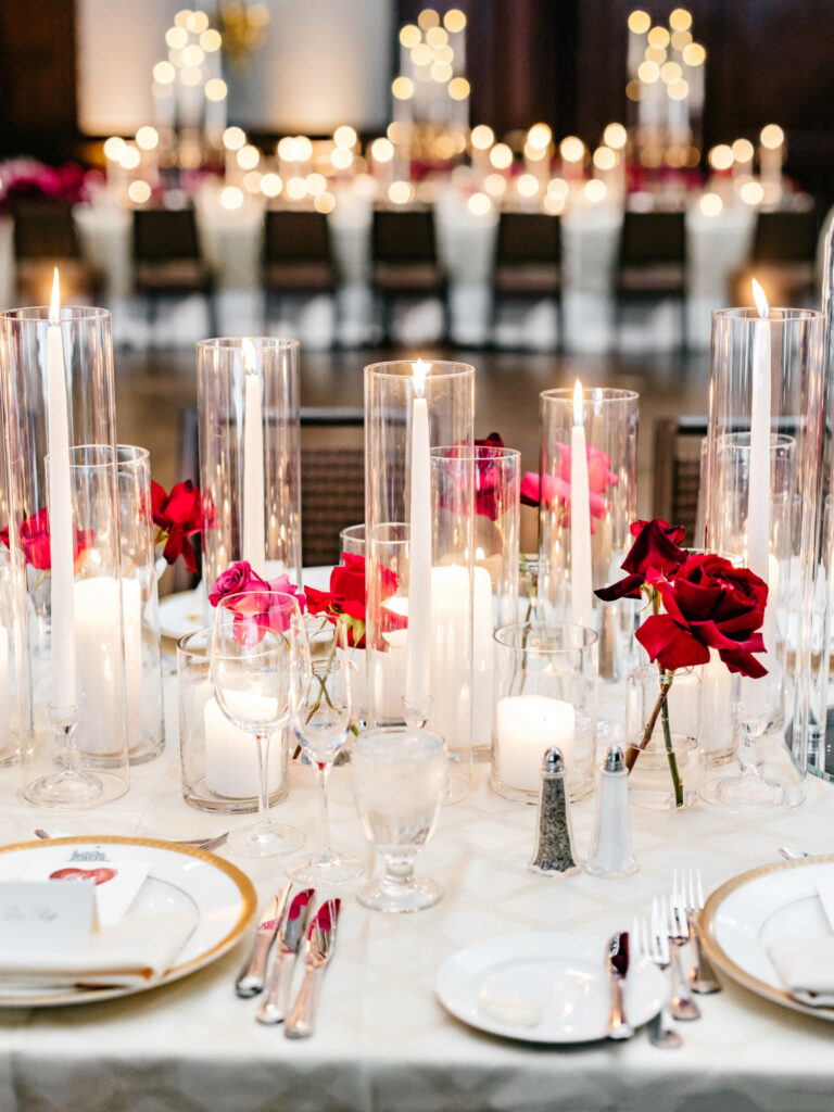 red and pink roses with long candles on luxurious wedding reception tablescape
