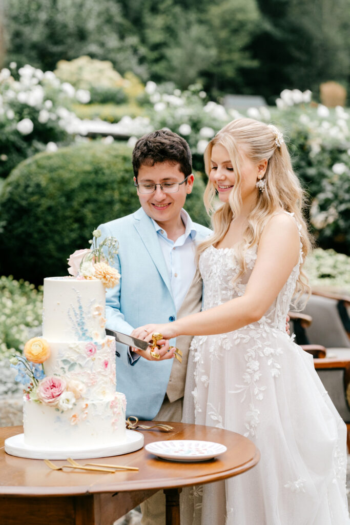 New Hampshire bride and groom cutting their 3 tier colorful floral wedding cake at their Uncanoonuc Mountain wedding reception