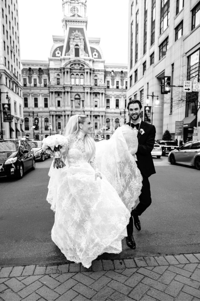 Philadelphia bride and groom walking down Broad Street in front of City Hall on their timeless wedding day by Emily Wren Photography