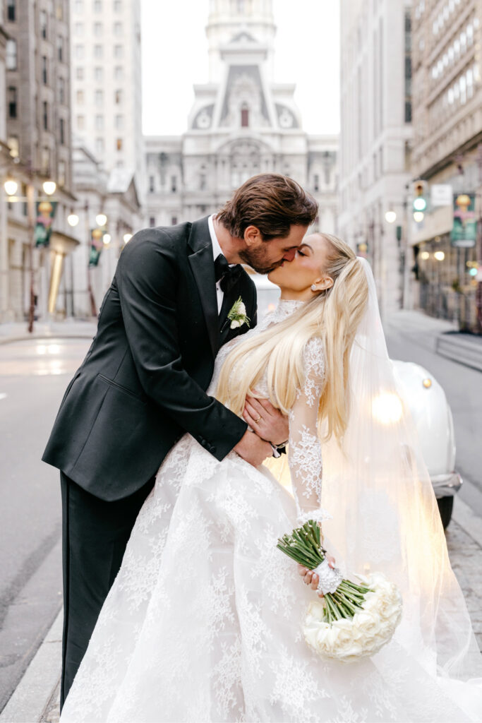 Philadelphia bride and groom kissing in front of a vintage Rolls-Royce car on Broad Street in front of City Hall by luxurious wedding photographer Emily Wren Photography