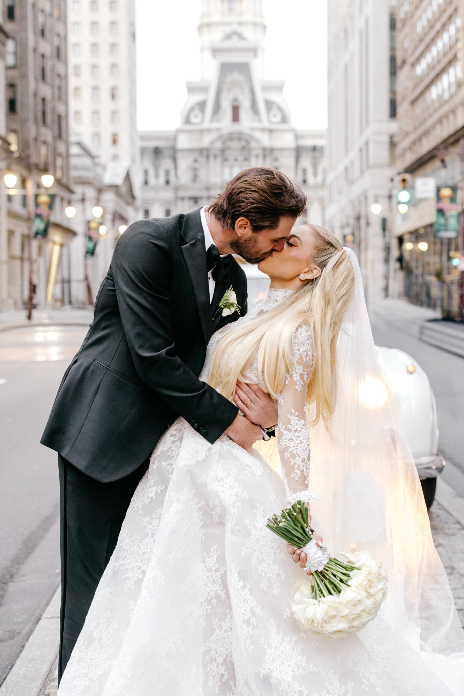 Philadelphia bride and groom kissing in front of a vintage Rolls-Royce car on Broad Street in front of City Hall by luxurious wedding photographer Emily Wren Photography