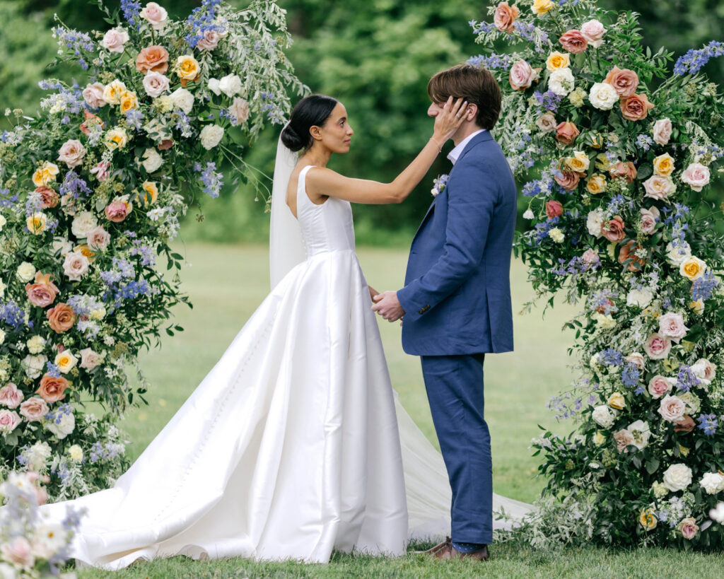 bride and groom at their outdoor wedding ceremony in front of a beautiful, colorful floral archway by elegant wedding photographer Emily Wren Photography