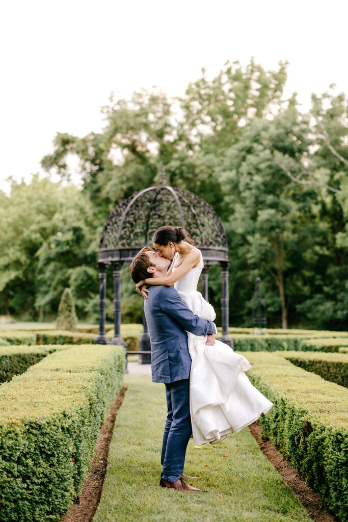 bride and groom kissing in a beautiful, manicured landscape on their summer garden wedding day in Philadelphia by Emily Wren Photography